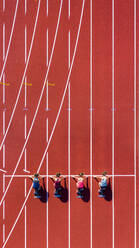 Germany, Baden-Wurttemberg, Winterbach, Aerial view of female sprinters kneeling on starting line - STSF02350