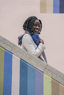 Porträt einer glücklichen jungen Frau mit schwarzen Zöpfen auf einer bunten Treppe - DLTSF00289
