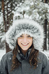 Portrait of happy young woman in winter forest by snowfall - OCMF00930