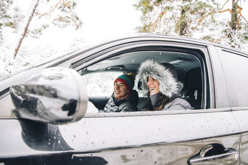 Happy young couple sitting in a car in winter forest having fun - OCMF00932
