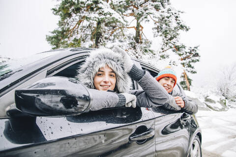 Porträt eines lächelnden jungen Paares, das sich im Winterwald aus dem Autofenster lehnt, lizenzfreies Stockfoto