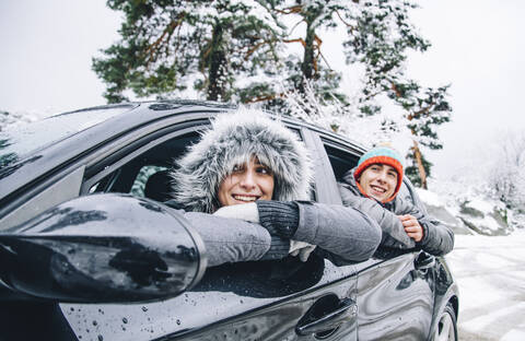 Porträt eines glücklichen jungen Paares, das in einem Auto im Winterwald sitzt und Spaß hat, lizenzfreies Stockfoto