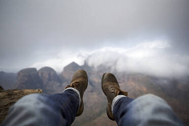 Mann mit einem Paar alter Stiefel auf dem Gipfel eines Hügels mit Blick auf den nebligen Blyde River Canyon, Südafrika - VEGF00873