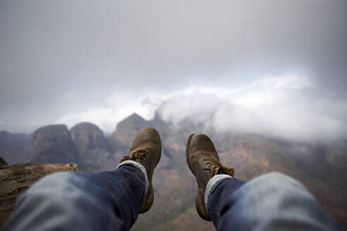 Man with a pair of vintage boots on the top of a hill overlooking the misty Blyde River Canyon, South Africa - VEGF00873