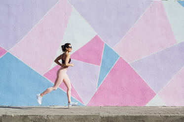 Mature woman running in front of a colorful wall - JCMF00301