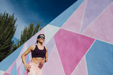 Mature woman running in front of a colorful wall - JCMF00303