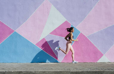 Mature woman running in front of a colorful wall - JCMF00304