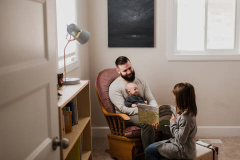 Mädchen im Wohnzimmer zeigt dem Vater und dem kleinen Bruder ein Buch, lizenzfreies Stockfoto