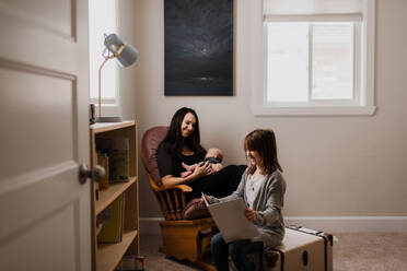 Junge Frau hält ihren kleinen Sohn im Wohnzimmersessel, während ihre Tochter ein Buch liest - ISF22989