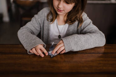 Girl at table folding paper, doing origami, head and shoulders - ISF22994