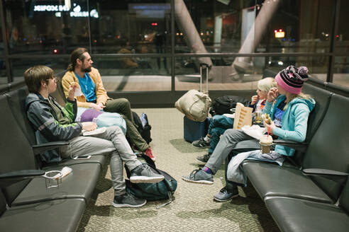 Älterer Mann mit Söhnen und Tochter wartet in der Abflughalle des Flughafens und isst Snacks - ISF23007