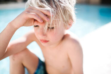 Blondhaariger Junge in Badeshorts sitzt mit geschlossenen Augen am Hotelpool, selektiver Fokus, Las Vegas, Nevada, USA - ISF23015