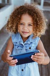 Kleines Mädchen benutzt Smartphone auf Veranda - ISF23104