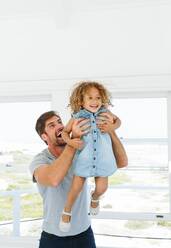 Father lifting daughter in mid air in beach house - ISF23120