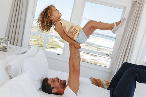 Vater hebt Tochter in der Luft auf Bett in Strandhaus - ISF23129