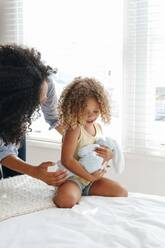 Woman talking to little girl cradling soft toy on bed - ISF23136