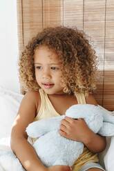 Little girl cradling soft toy, daydreaming in bed - ISF23137