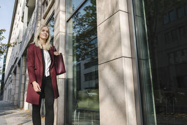 Blonde Geschäftsfrau mit Smartphone im Hintergrund moderne Gebäude - AHSF01355