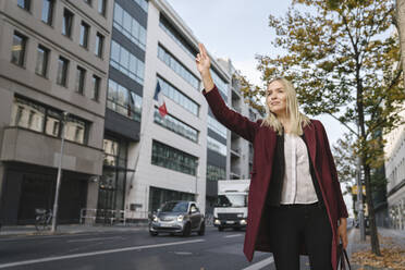 Blond businesswoman in the city hailing a taxi - AHSF01356