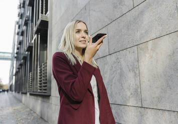 Blonde Geschäftsfrau mit Smartphone in der Stadt - AHSF01358