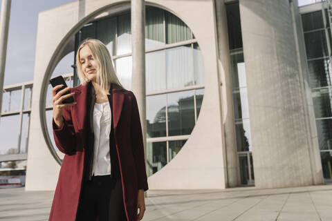 Blonde Geschäftsfrau mit Smartphone im Hintergrund modernen Gebäude, lizenzfreies Stockfoto
