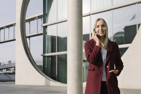 Blonde Geschäftsfrau mit Smartphone im Hintergrund modernen Gebäude - AHSF01367