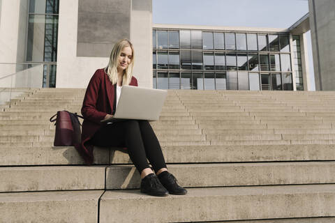 Blonde Geschäftsfrau mit Laptop im Hintergrund eines modernen Bürogebäudes, lizenzfreies Stockfoto