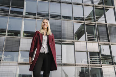 Blonde Geschäftsfrau mit Laptop im Hintergrund eines modernen Bürogebäudes - AHSF01377