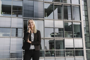 Blonde Geschäftsfrau mit Smartphone im Hintergrund modernen Gebäude - AHSF01378