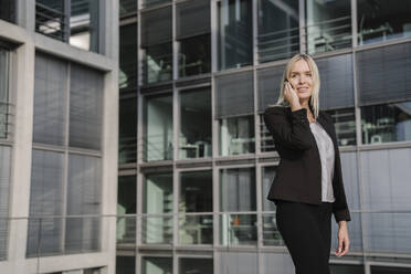 Blonde Geschäftsfrau mit Smartphone im Hintergrund modernen Gebäude - AHSF01381