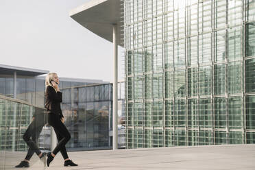 Blonde Geschäftsfrau mit Smartphone im Hintergrund moderne Gebäude - AHSF01384