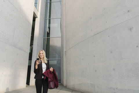 Blonde Geschäftsfrau mit Smartphone im Hintergrund moderne Gebäude, lizenzfreies Stockfoto