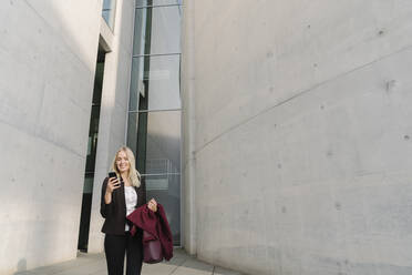 Blond businesswoman using smartphone in the background modern buildings - AHSF01385