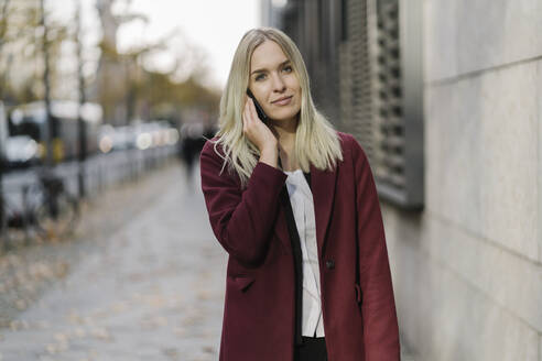 Blonde Geschäftsfrau mit Smartphone im Hintergrund modernen Gebäude - AHSF01390