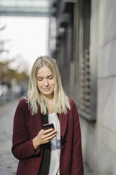 Blonde Geschäftsfrau mit Smartphone in der Stadt, Blick nach unten - AHSF01391