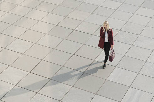 View from above of blond businesswoman using smartphone, walking on concrete ground - AHSF01394