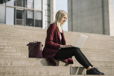 Blonde Geschäftsfrau mit Laptop, auf einer Stufe sitzend - AHSF01399