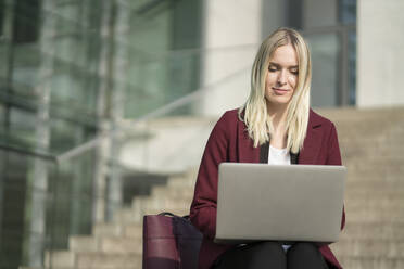 Blonde Geschäftsfrau mit Laptop, auf einer Stufe sitzend - AHSF01400