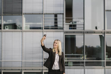 Blonde Geschäftsfrau, die ein Smartphone benutzt und ein Selfie macht - AHSF01405