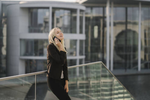 Blonde Geschäftsfrau mit Smartphone im Hintergrund modernen Gebäude - AHSF01406