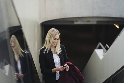 Blonde Geschäftsfrau benutzt Smartphone bei der Benutzung der Rolltreppe, lizenzfreies Stockfoto