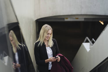 Blonde Geschäftsfrau benutzt Smartphone bei der Benutzung der Rolltreppe - AHSF01407