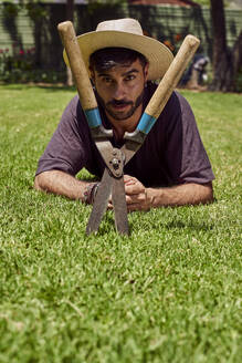 Portrait of man with pruner lying on lawn in garden - VEGF00888