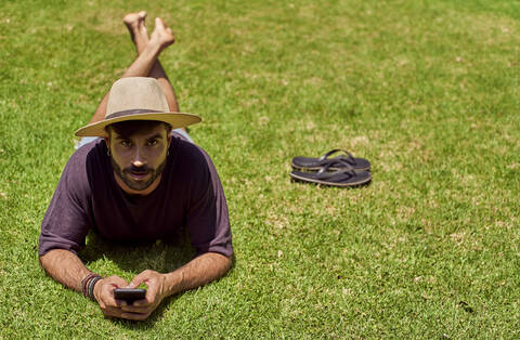 Mann liegt im Gras und benutzt sein Smartphone, lizenzfreies Stockfoto