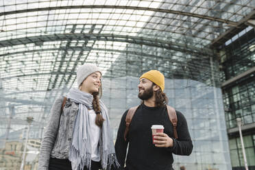Glückliches junges Paar mit Kaffee zum Mitnehmen am Hauptbahnhof, Berlin, Deutschland - AHSF01413
