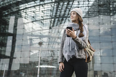 Junge Frau mit Smartphone beim Warten am Hauptbahnhof, Berlin, Deutschland - AHSF01419