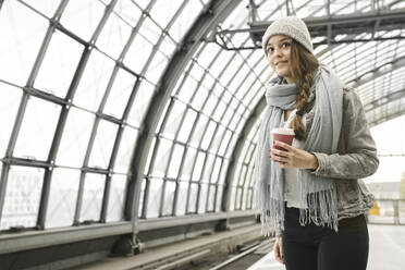 Junge Frau mit Kaffee zum Mitnehmen wartet am Bahnsteig, Berlin, Deutschland - AHSF01424