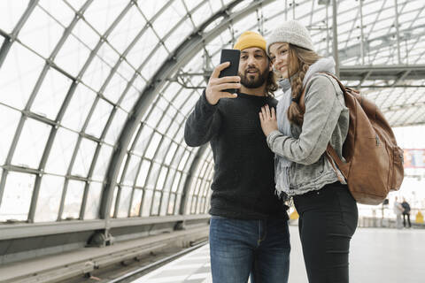 Glückliches junges Paar mit Smartphone auf dem Bahnsteig, Berlin, Deutschland, lizenzfreies Stockfoto