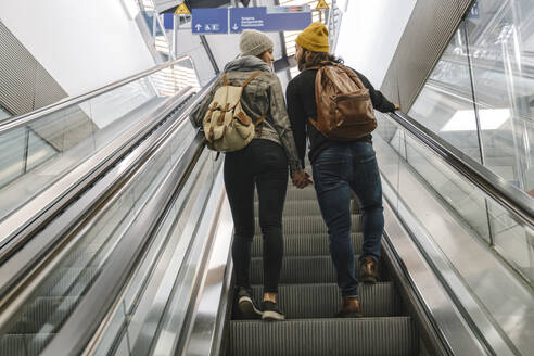 Rückansicht eines jungen Paares auf einer Rolltreppe am Bahnhof, Berlin, Deutschland - AHSF01446