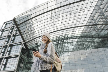 Glückliche junge Frau mit Smartphone am Hauptbahnhof, Berlin, Deutschland - AHSF01484